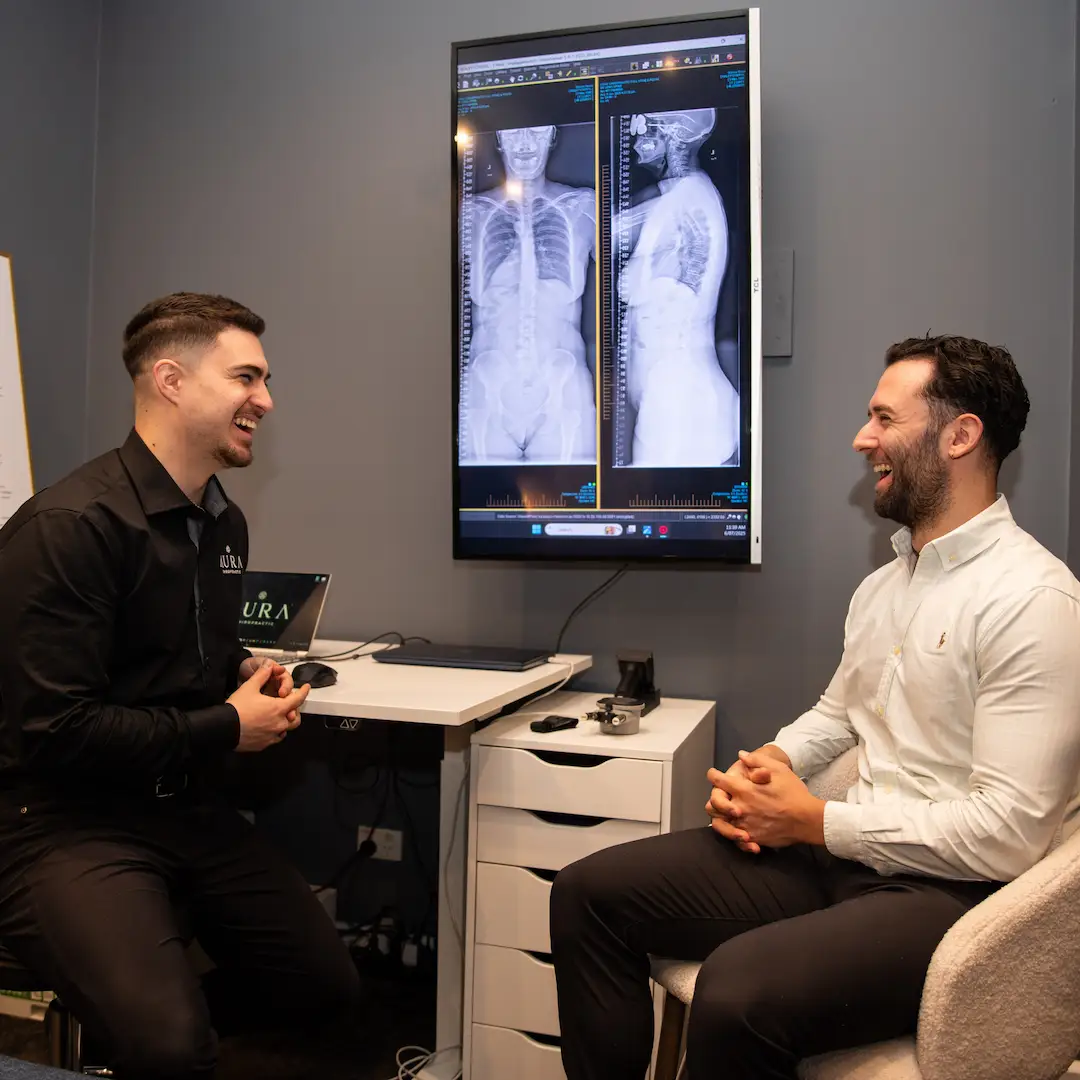 Dr Arthur Kaganovitch and a patient sitting inside Aura Chiropractic laughing together. This patient is suffering from neck or back pain and feels a lot better since seeing Dr Arthur.